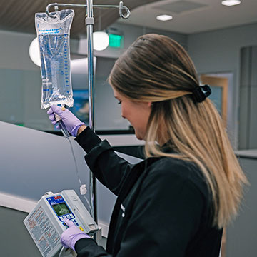 A nurse in black scrubs prepares an infusion bag for a patient.